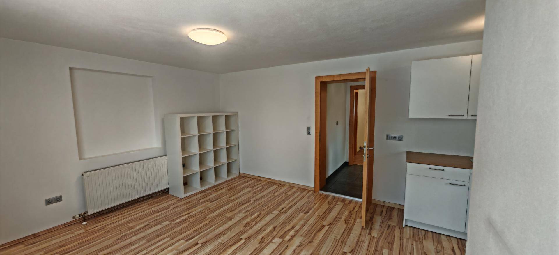 Zimmer mit Holzboden, Regal und kleiner Küchenzeile, ideal als Gästezimmer oder Büro.