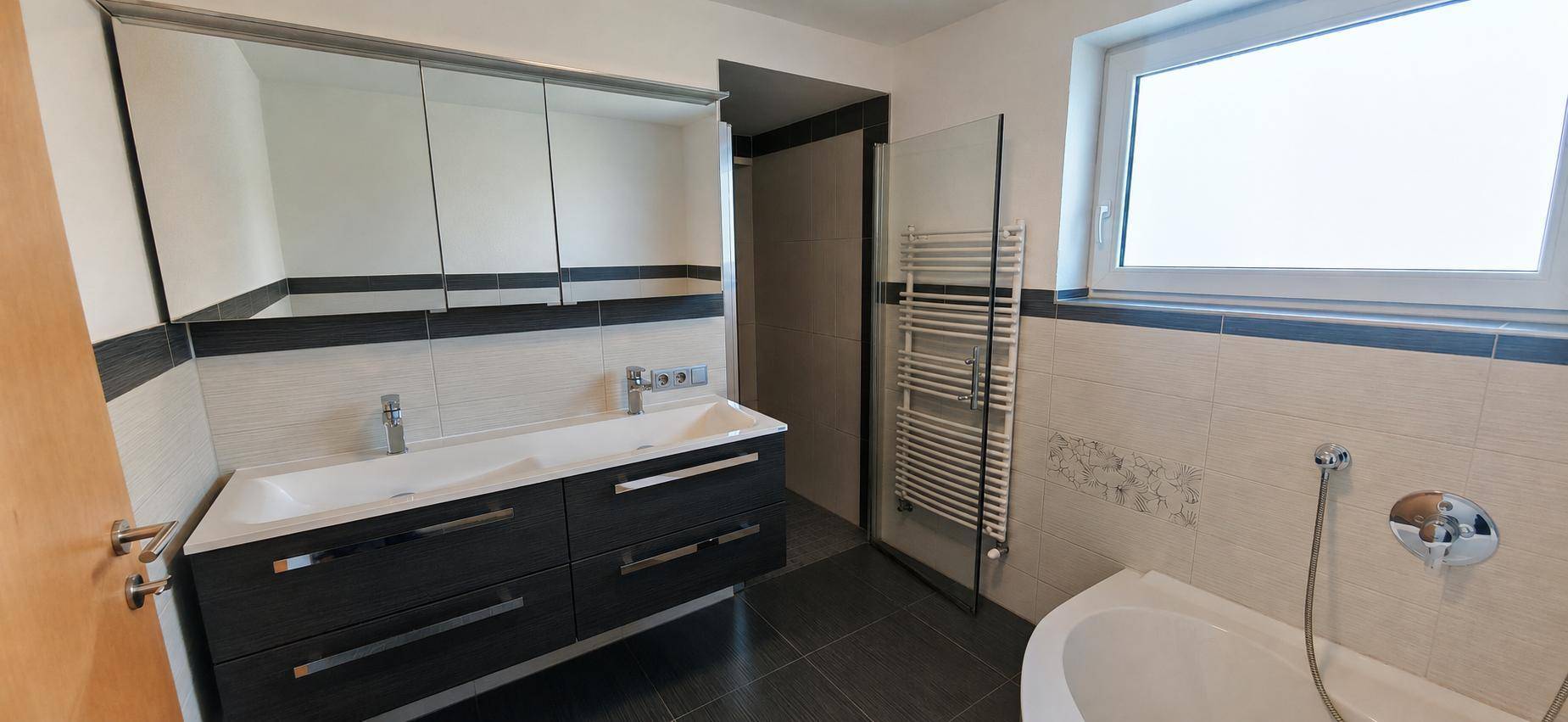 Modernes Badezimmer mit Doppelwaschbecken, Badewanne, beheiztem Handtuchhalter und Fenster.