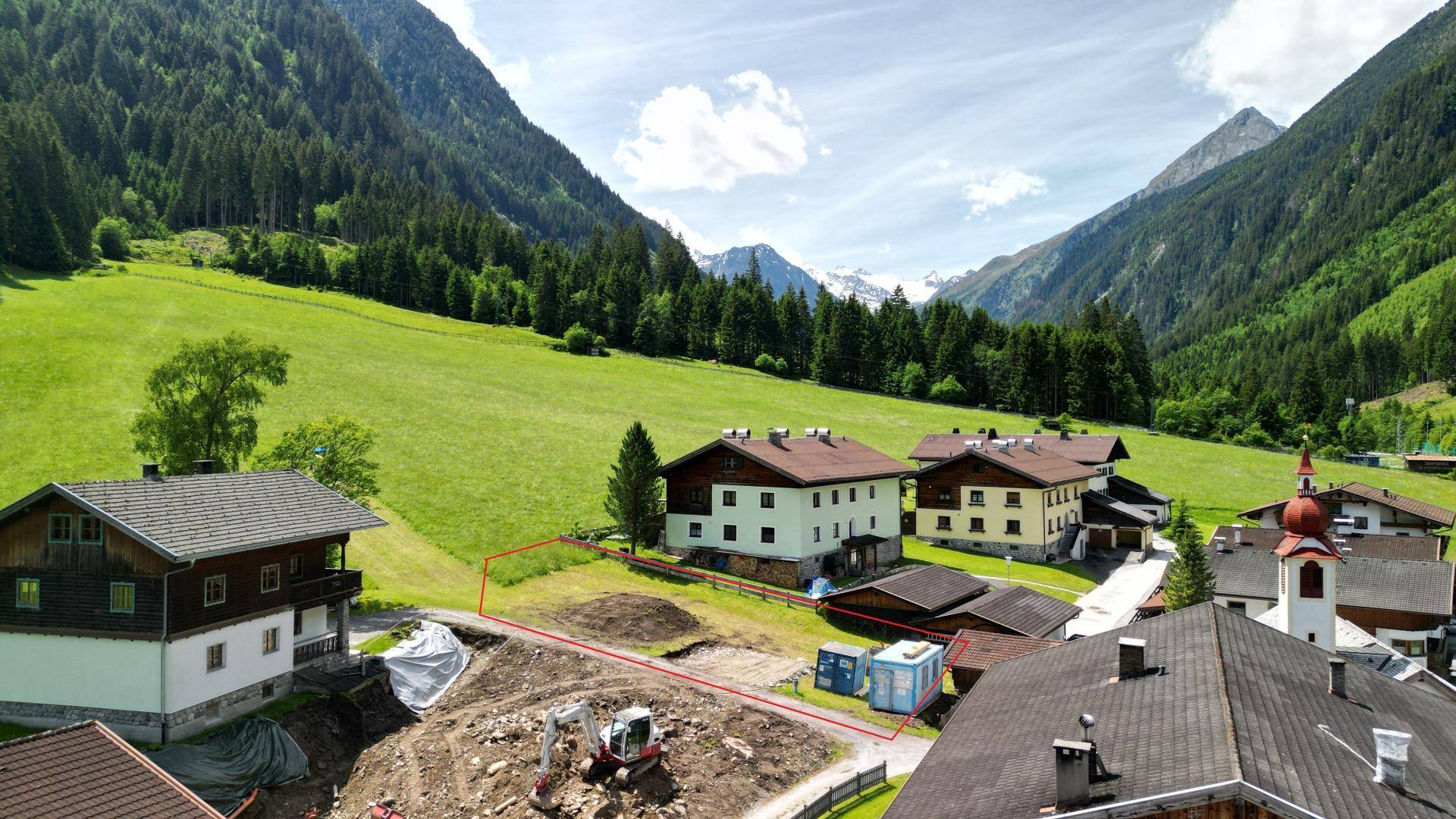 Übersicht des Dorfes und der umliegenden Bergwelt, mit einem rot umrandeten Baugrundstück im Vordergrund.