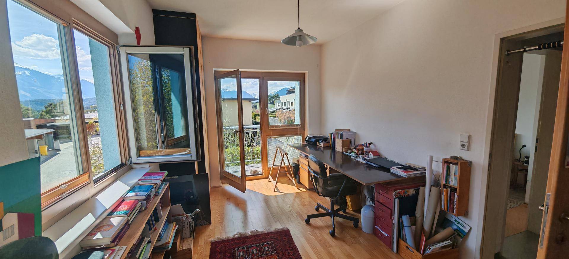 Arbeitszimmer mit Schreibtisch, Bücherregalen und Balkonzugang mit Bergblick.