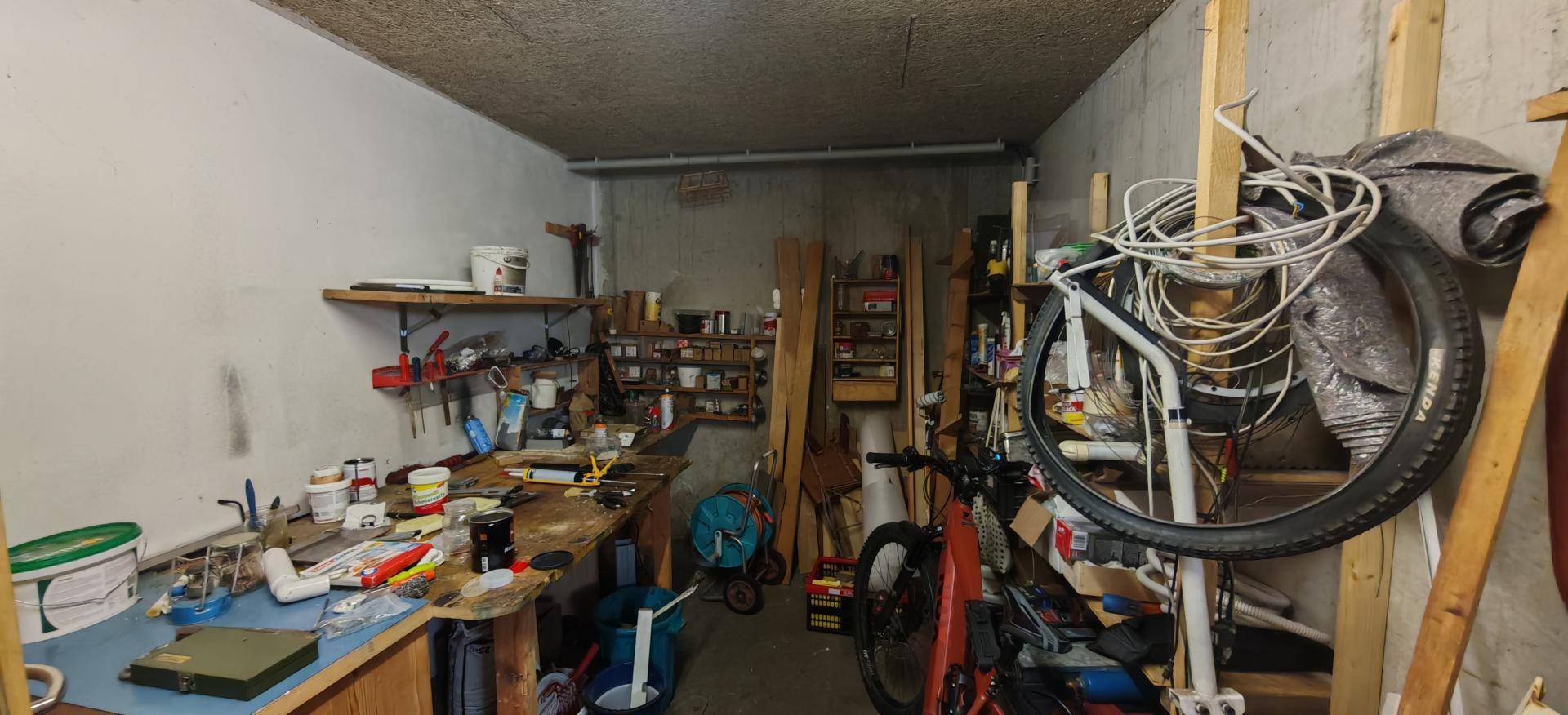 Werkstatt im Keller mit Werkbank, Regalen und Stauraum für Fahrräder.