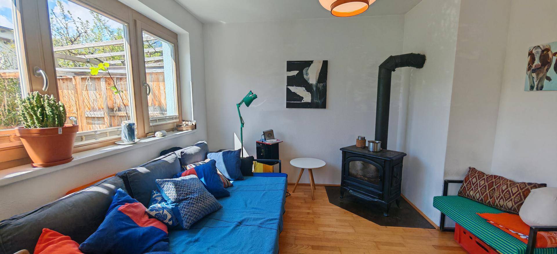 Helles Wohnzimmer mit Sofa, Kaminofen und großem Fenster zum Garten.