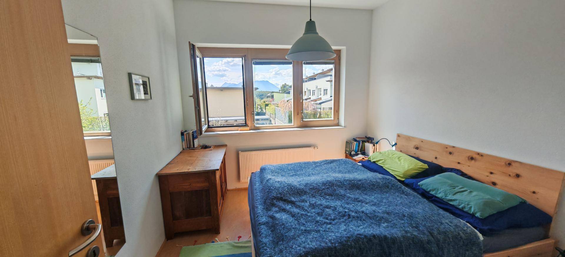Schlafzimmer mit Holzbett, Kommode und Fenster mit Blick auf die Berge.
