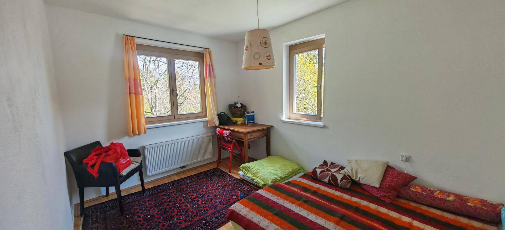 Schlafzimmer mit Einzelbett, Schreibtisch und zwei Fenstern für natürliche Belichtung.