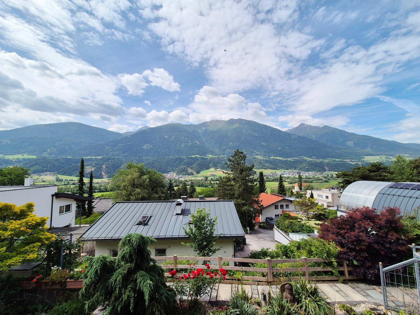 Weitläufiger Blick über die umliegende Landschaft mit Häusern, viel Grün und majestätischen Bergen.