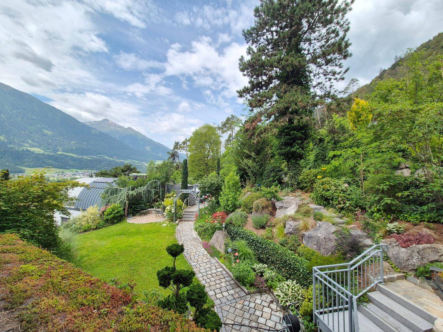 Großzügiger, terrassierter Garten mit Steinpfaden, vielfältiger Bepflanzung und Bergblick.