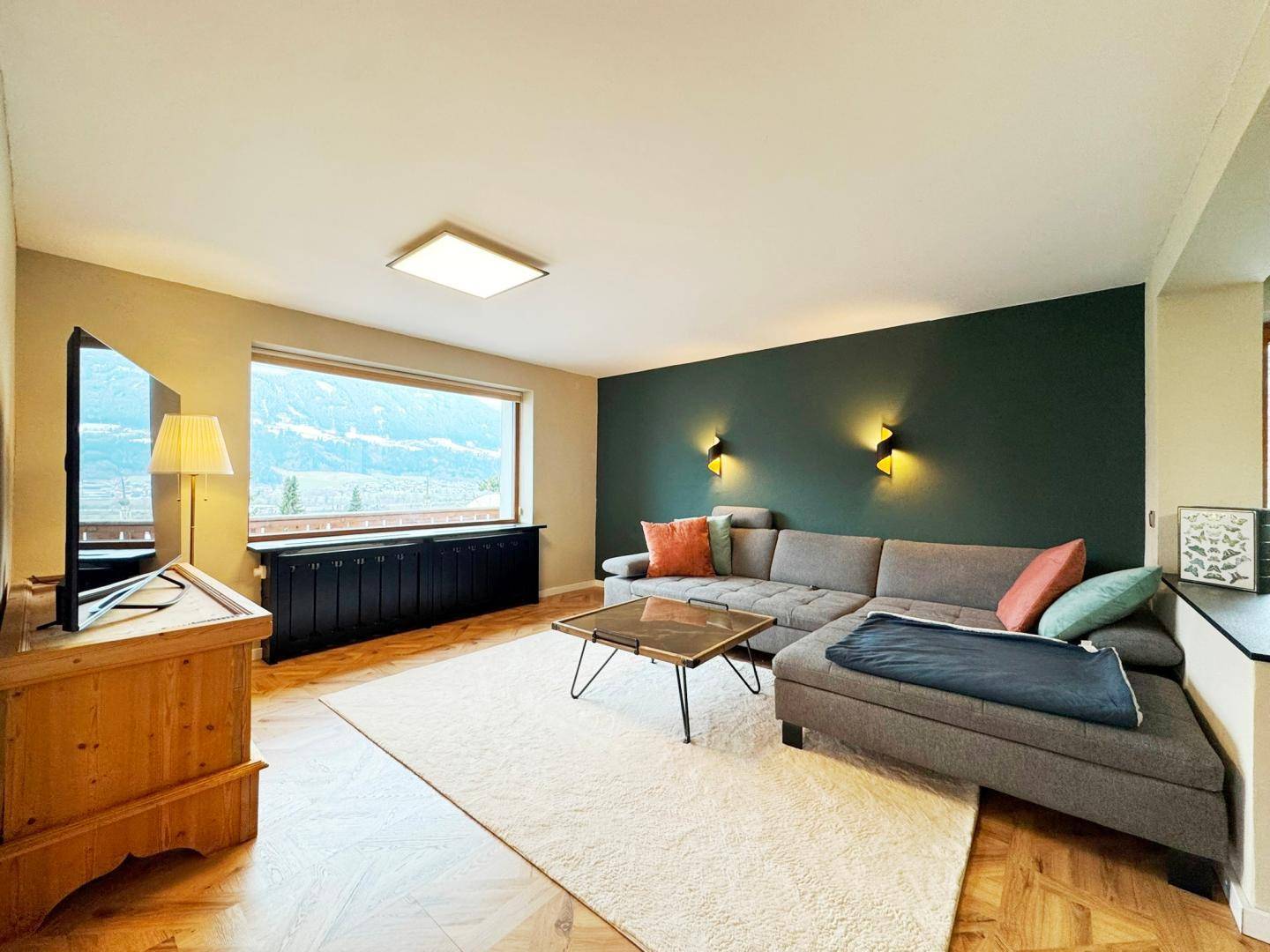Gemütliches Wohnzimmer mit großem Sofa, Holzboden und weitem Blick auf die Berglandschaft.