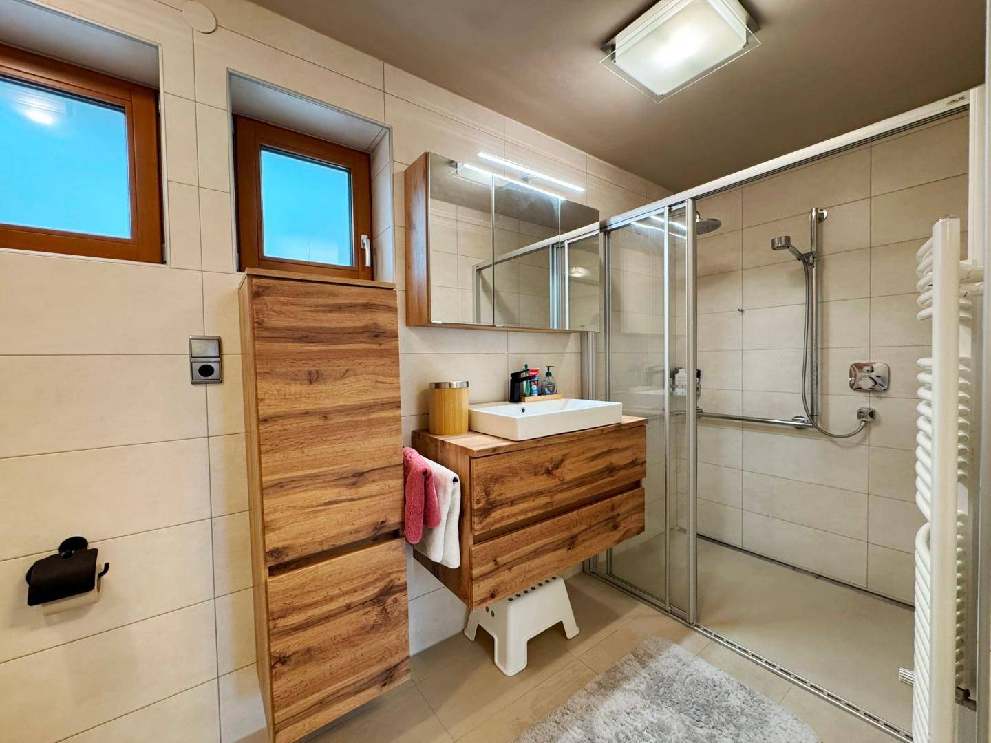 Modernes Badezimmer mit Holzwaschtisch, ebenerdiger Dusche und beheiztem Handtuchhalter.