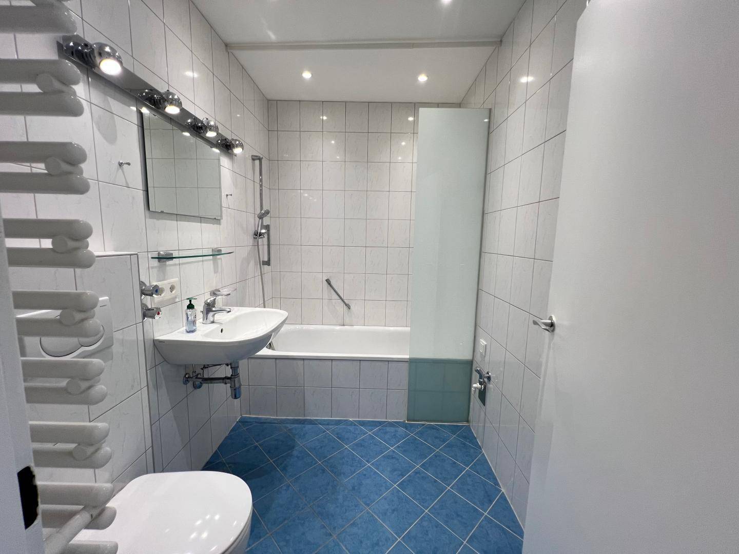 Badezimmer mit blauen Fliesen, Badewanne mit Duschwand und beheiztem Handtuchhalter.