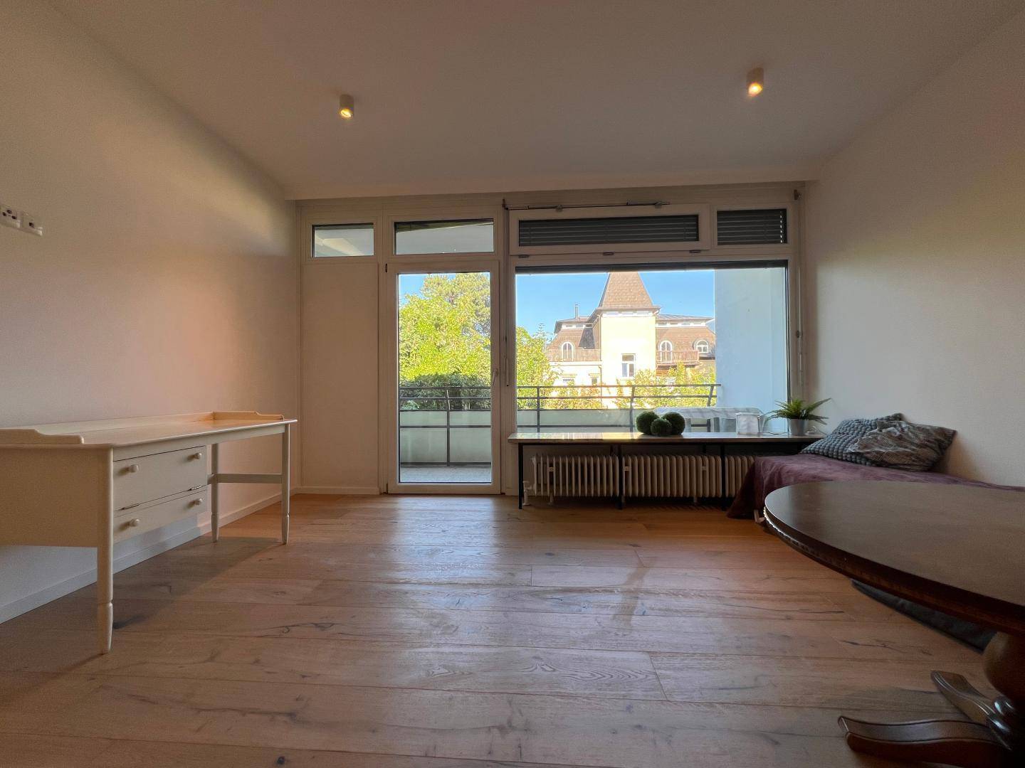 Heller Wohnraum mit Holzboden, großen Fenstern und Zugang zu einem Balkon mit Stadtblick.