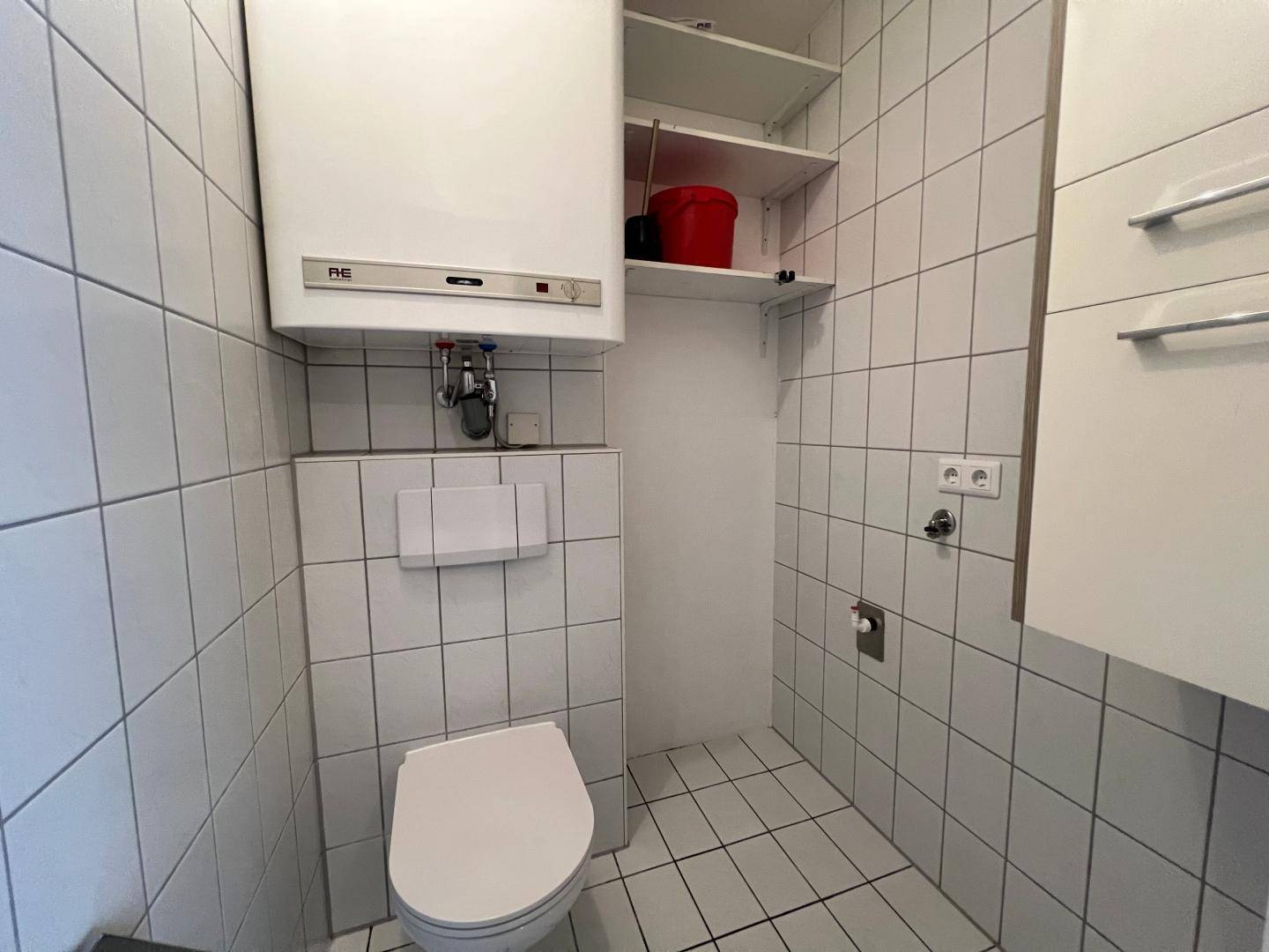 Kleines WC mit Toilette, Boiler und vollständig gefliesten Wänden.
