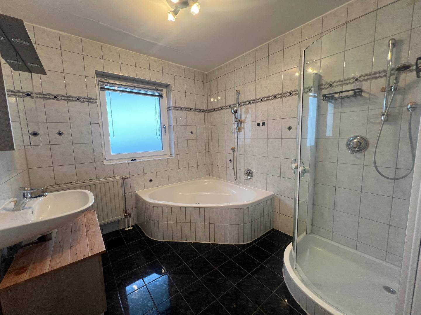 Gefliestes Badezimmer mit Eckbadewanne, separater Duschkabine und Fenster.