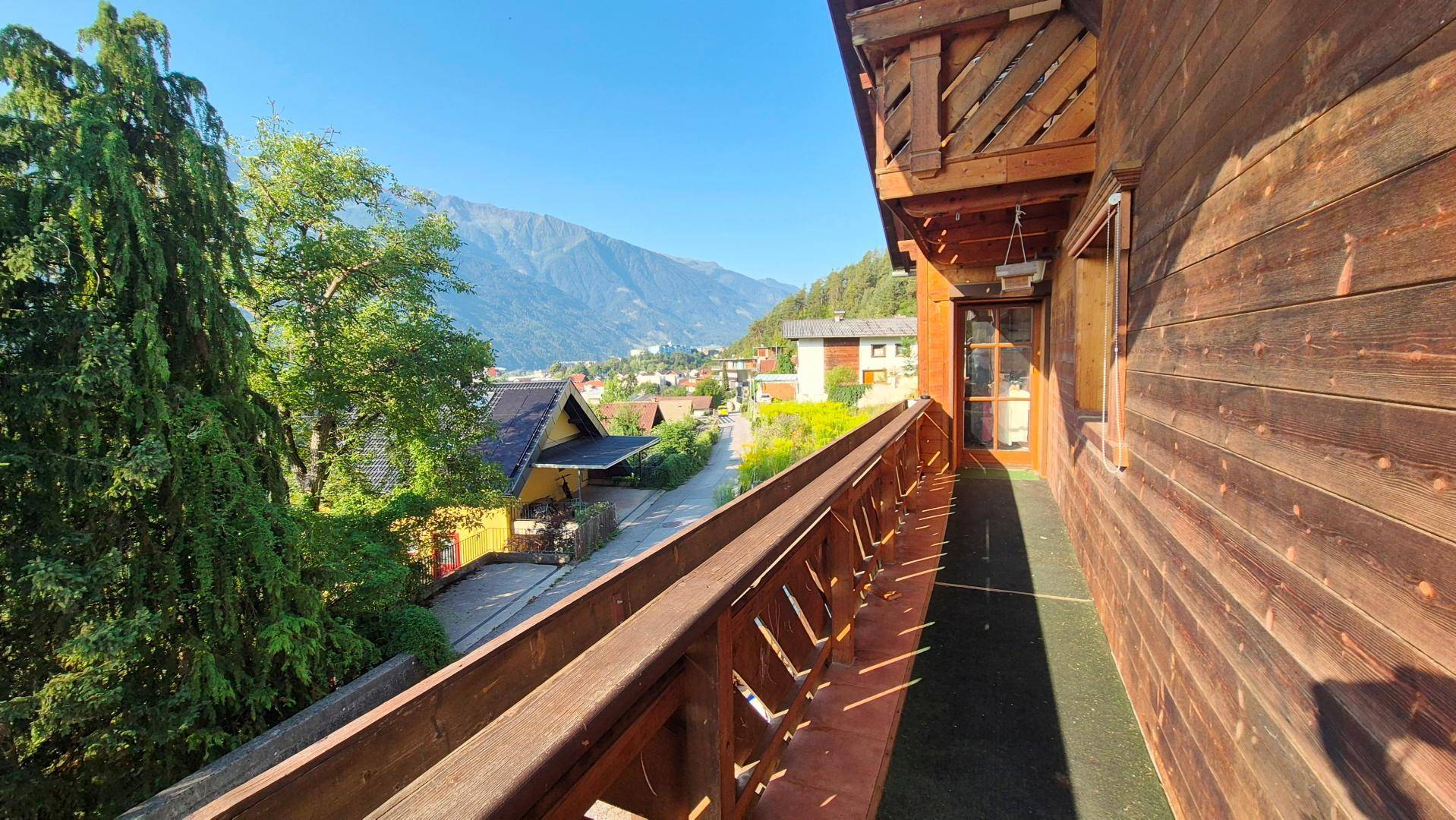 Langer Holzbalkon mit traditionellem Geländer und Panoramablick auf die Berge.