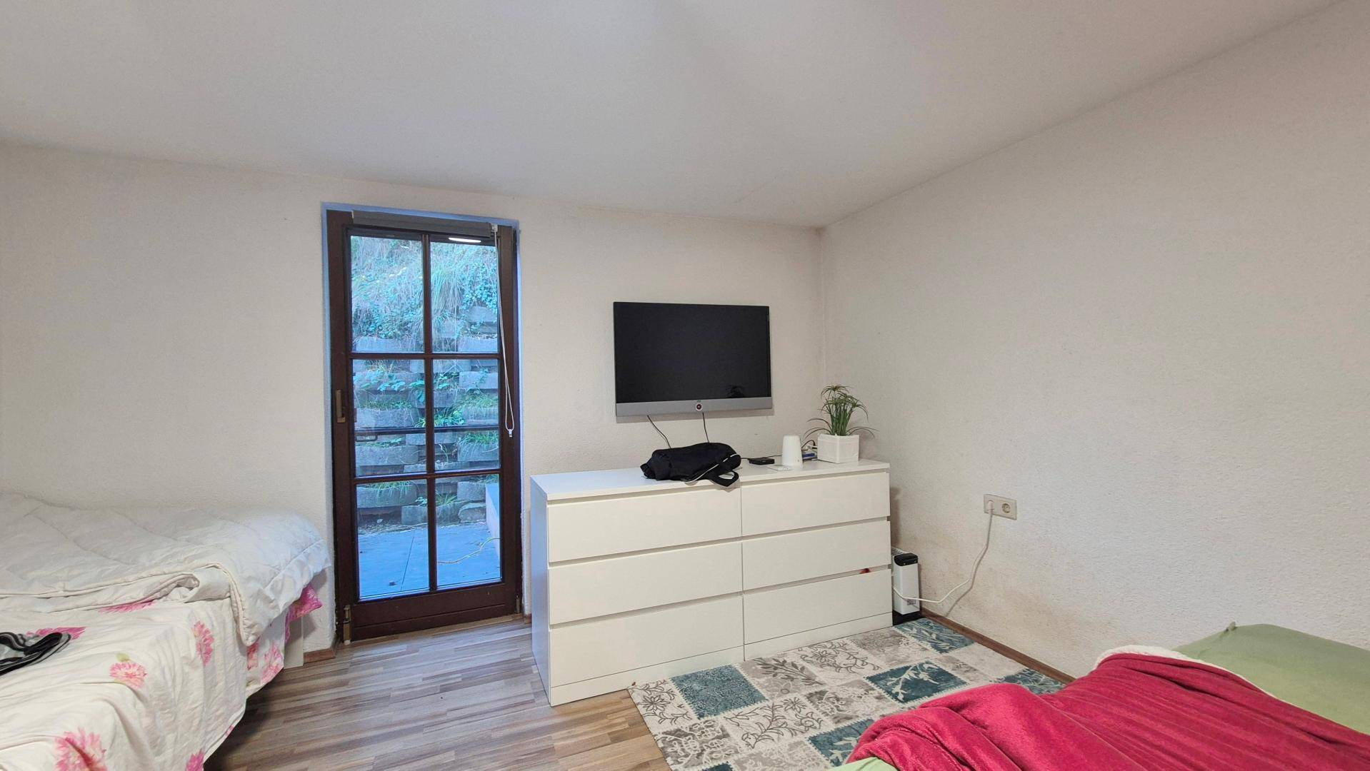 Schlafzimmer mit zwei Betten, einer Kommode und Zugang zu einem Außenbereich.