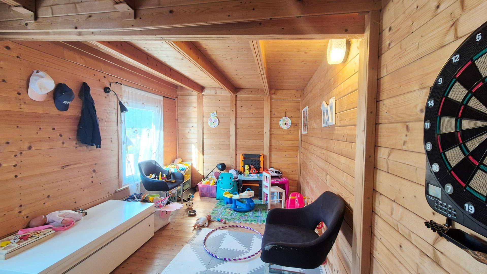 Rustikales Kinderzimmer mit Holzvertäfelung, Spielzeug und einem Dartboard an der Wand.