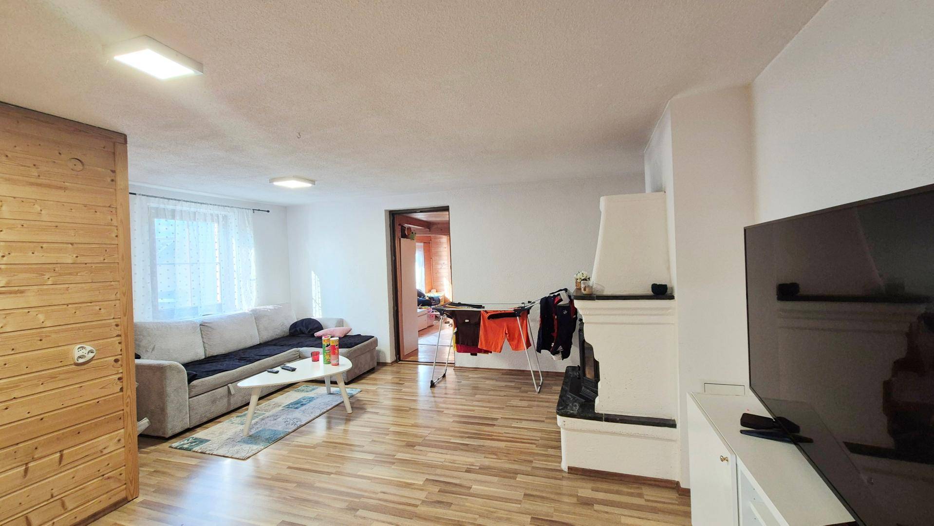 Gemütliches Wohnzimmer mit Holzboden, Sofa und einem traditionellen Kaminofen.