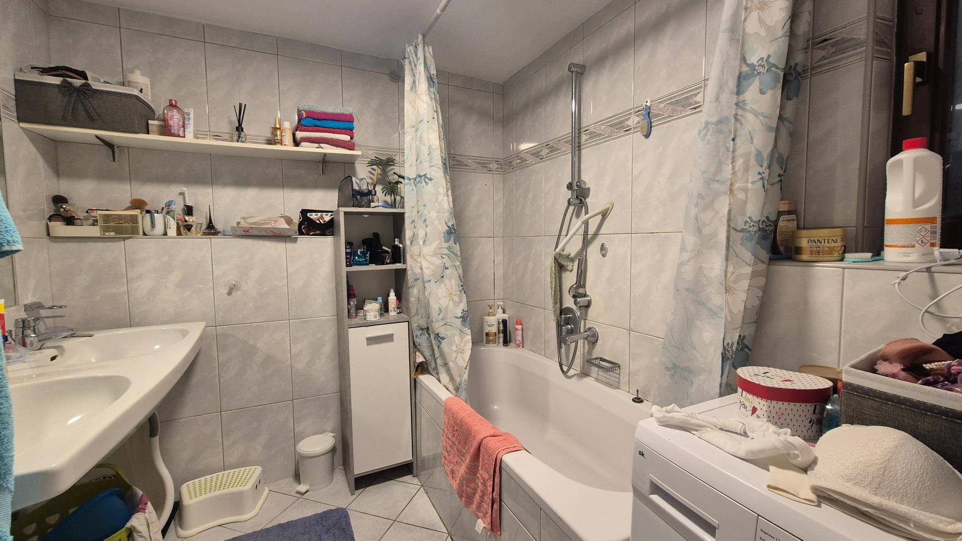 Gefliestes Badezimmer mit Badewanne, Duschvorhang und Waschbecken, in gutem Zustand.
