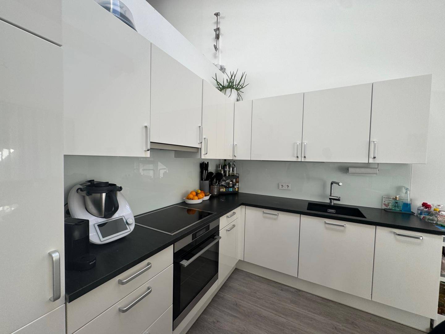Moderne Küche mit weißen Hochglanzschränken, schwarzer Arbeitsplatte und Induktionskochfeld.