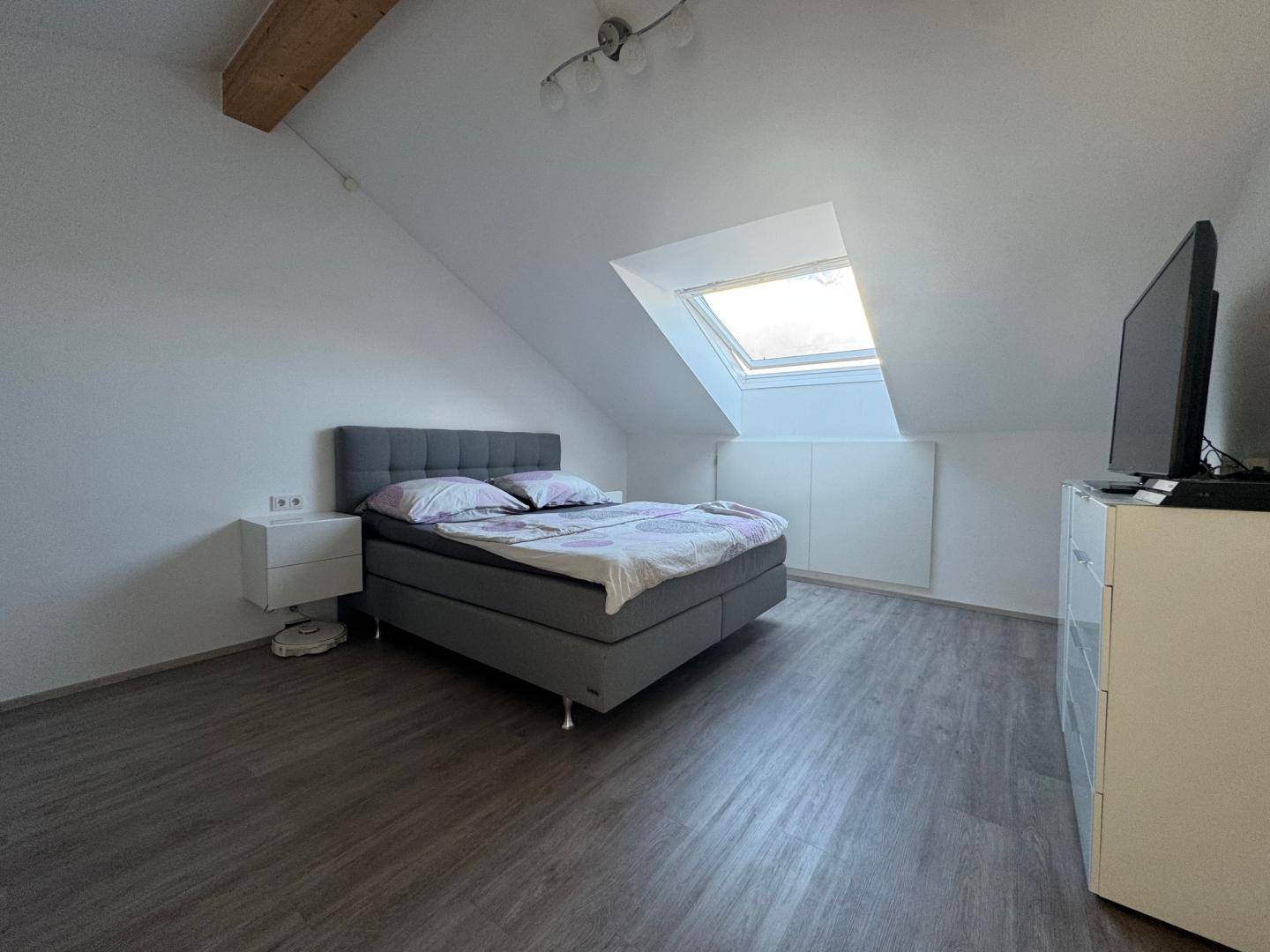Gemütliches Schlafzimmer im Dachgeschoss mit Dachfenster, Holzbalken und modernem Bett.