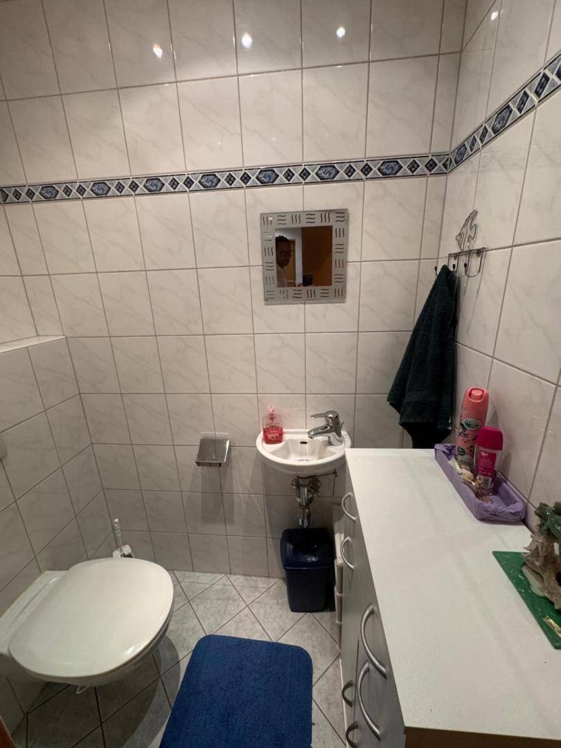 Kleines Gäste-WC mit weißen Fliesen, einem Waschbecken und WC.