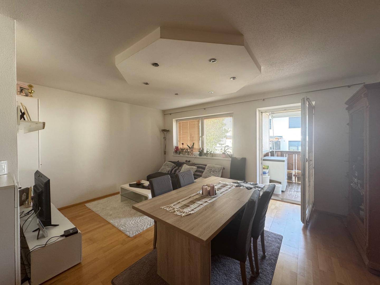Gemütlicher Wohn-Essbereich mit Holzboden und direktem Zugang zum sonnigen Balkon.