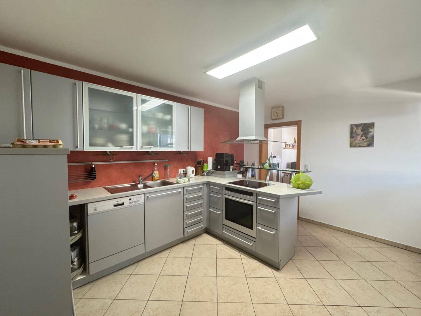 Moderne Einbauküche mit grauen Fronten, integrierten Geräten und Fliesenboden.