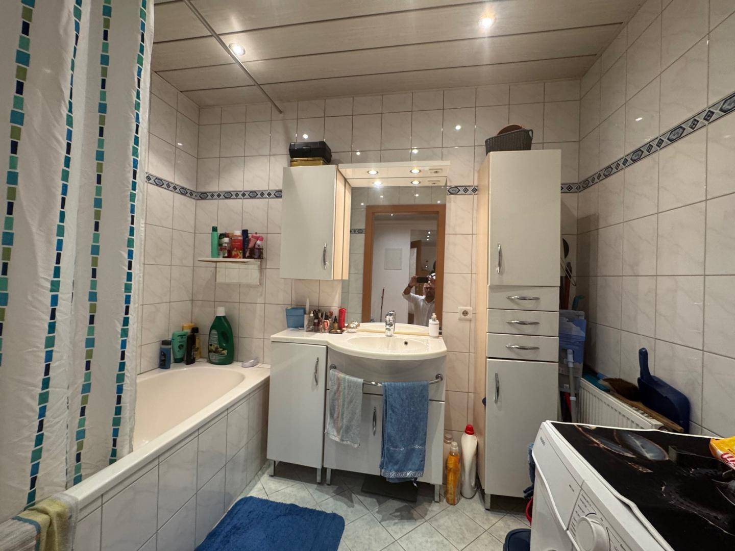 Badezimmer mit Badewanne, Waschbecken, Spiegelschrank und hellen Fliesen.
