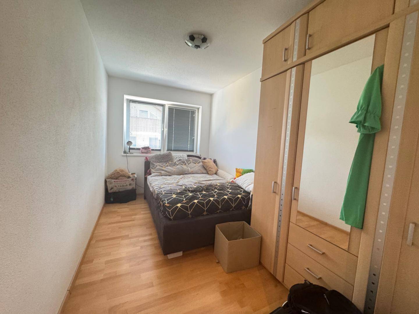 Kleines Schlafzimmer mit Einzelbett, Holzboden und einem Spiegelschrank.