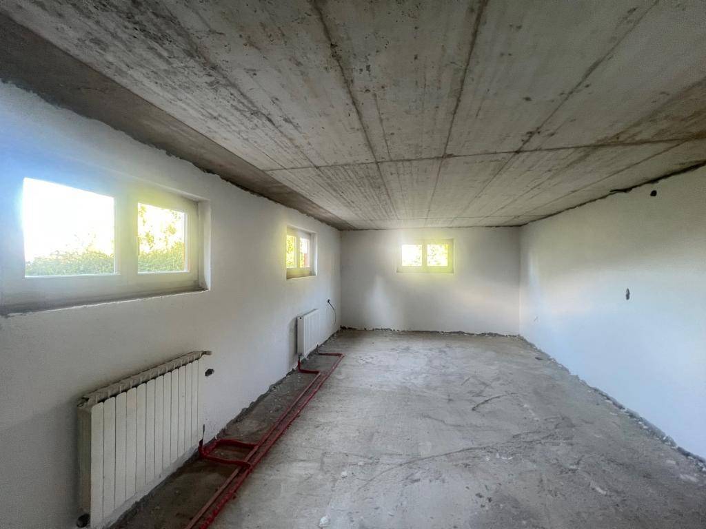 Unfertiger Kellerraum mit Betonboden, weißen Wänden, Fenstern und Heizkörpern.