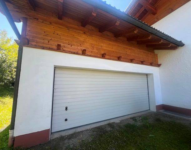 Garagentor aus Metall an einem Gebäude mit Holzverkleidung und weißer Fassade.