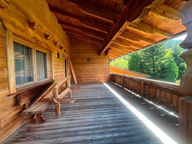 Geräumiger Holzbalkon mit traditionellen Sitzbänken und Blick ins Grüne.