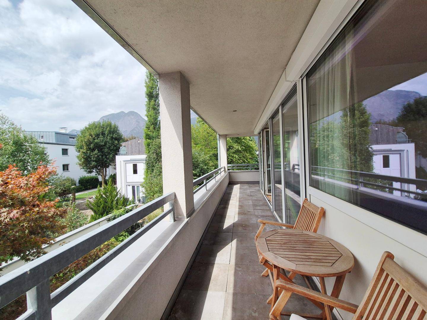 Langer Balkon mit Holztisch und Stühlen, der einen malerischen Blick auf die Berge bietet.