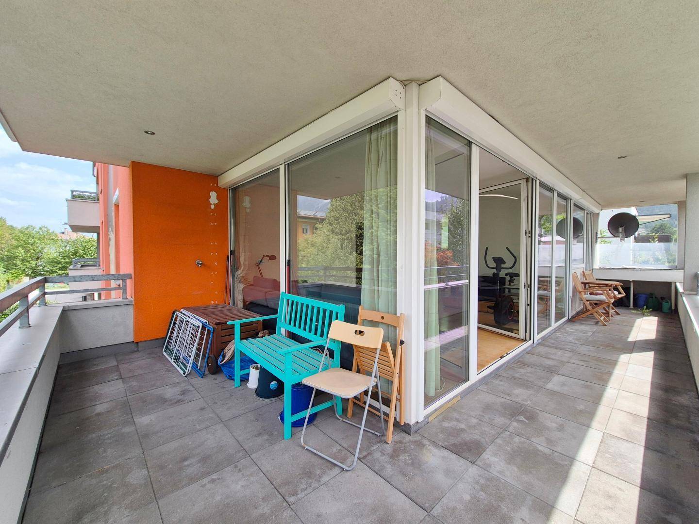 Geräumiger Balkon mit Fliesenboden, Sitzgelegenheiten und großen Glasfronten zum Innenbereich.