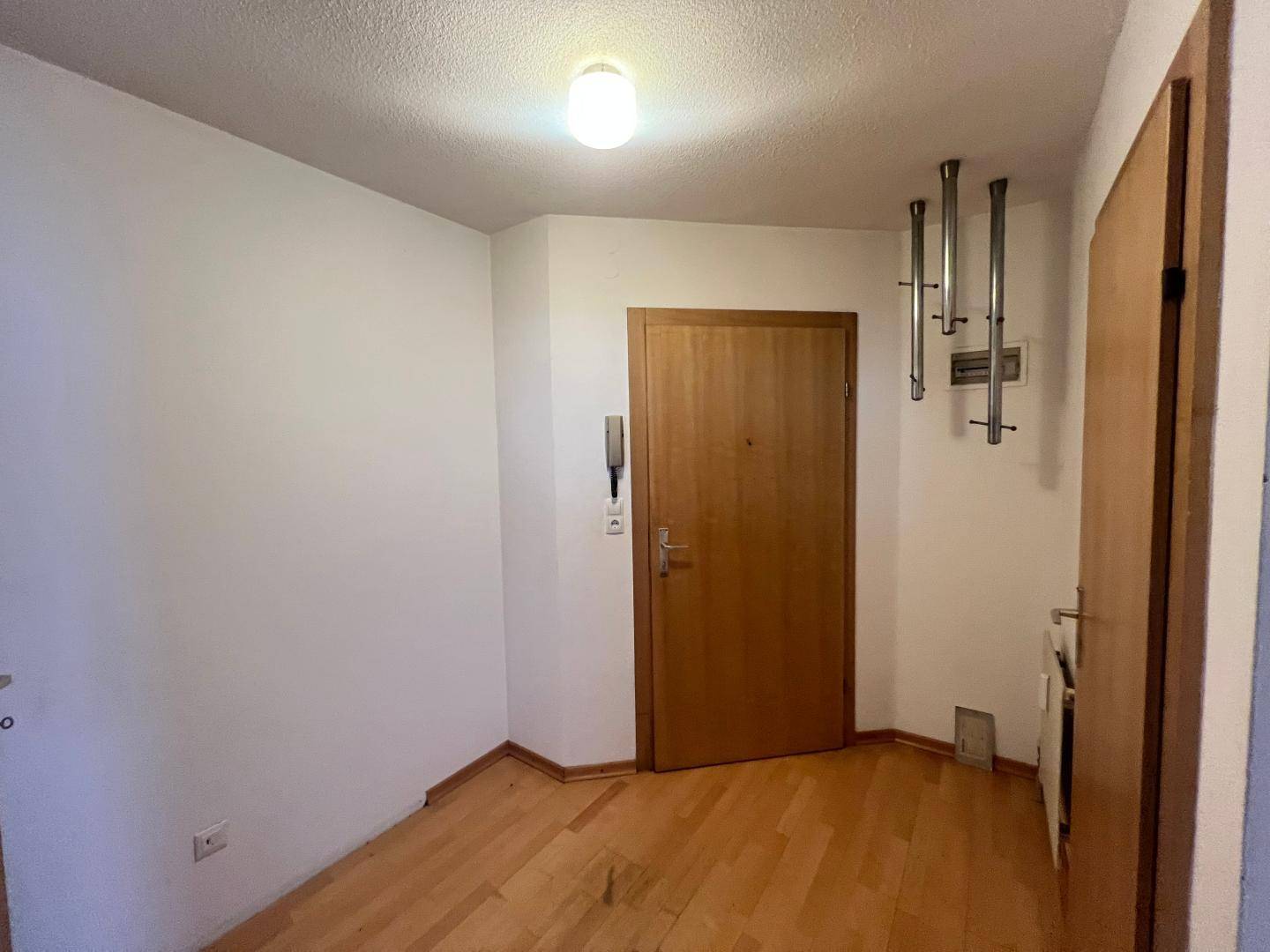 Eingangsbereich mit Holztür, Gegensprechanlage und einem modernen Garderobenständer.