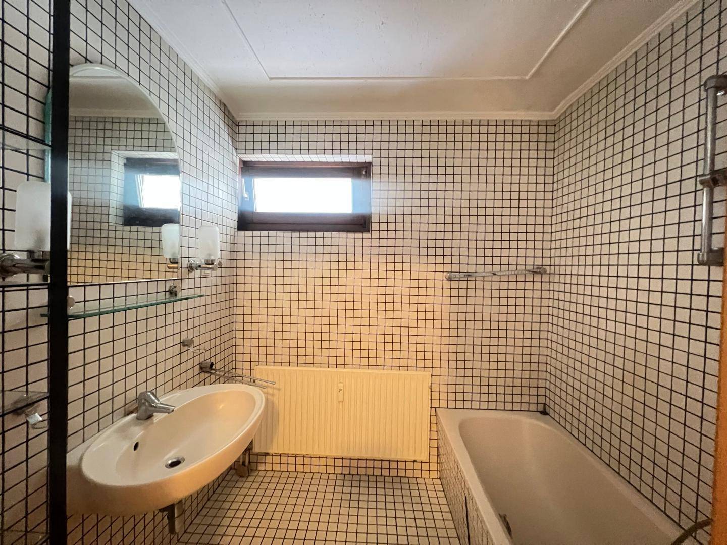 Badezimmer mit kleinen schwarz-weißen Fliesen, Badewanne, Waschbecken und einem Fenster.