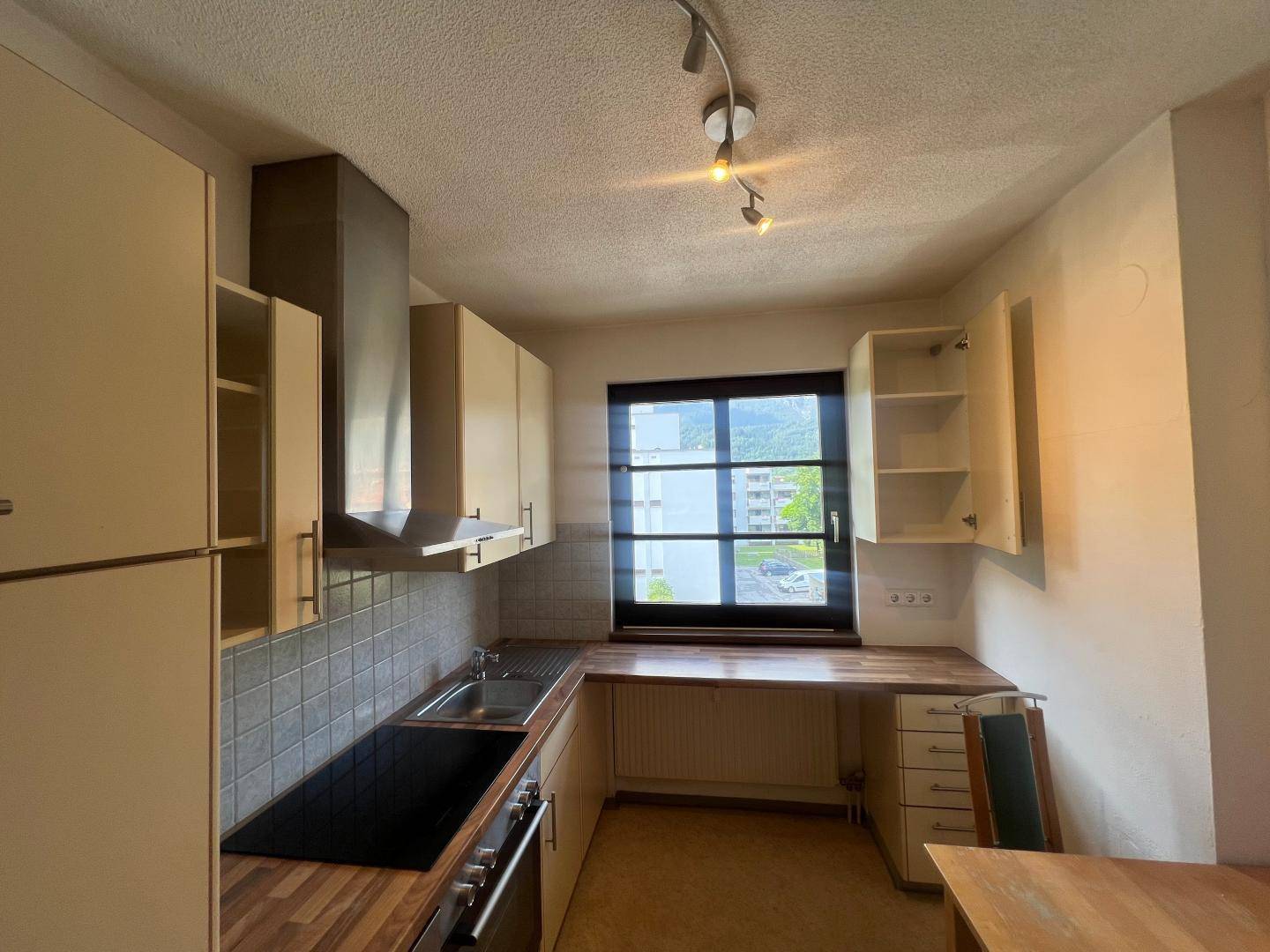 Funktionale Küche mit U-förmiger Anordnung, Fenster, Spüle, Kochfeld und Dunstabzugshaube.