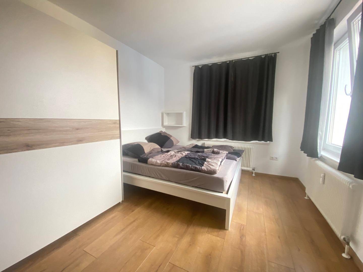 Schlafzimmer mit Doppelbett, großem Kleiderschrank und Fenster mit dunklen Vorhängen.