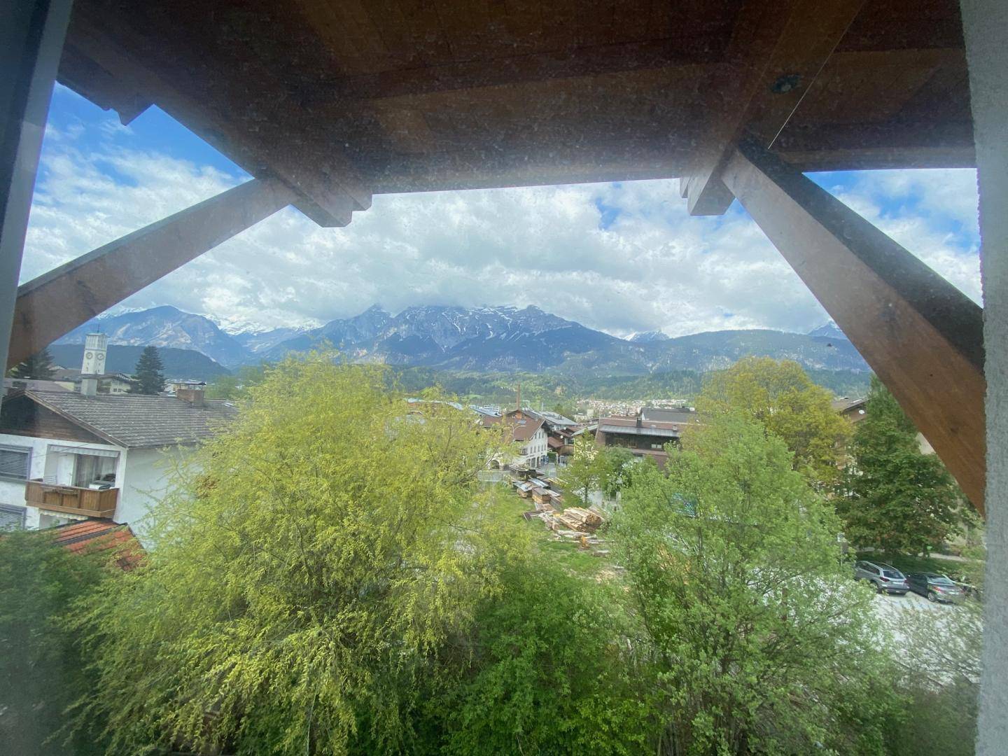 Malerischer Bergblick aus dem Fenster mit grünen Bäumen und Häusern im Vordergrund.
