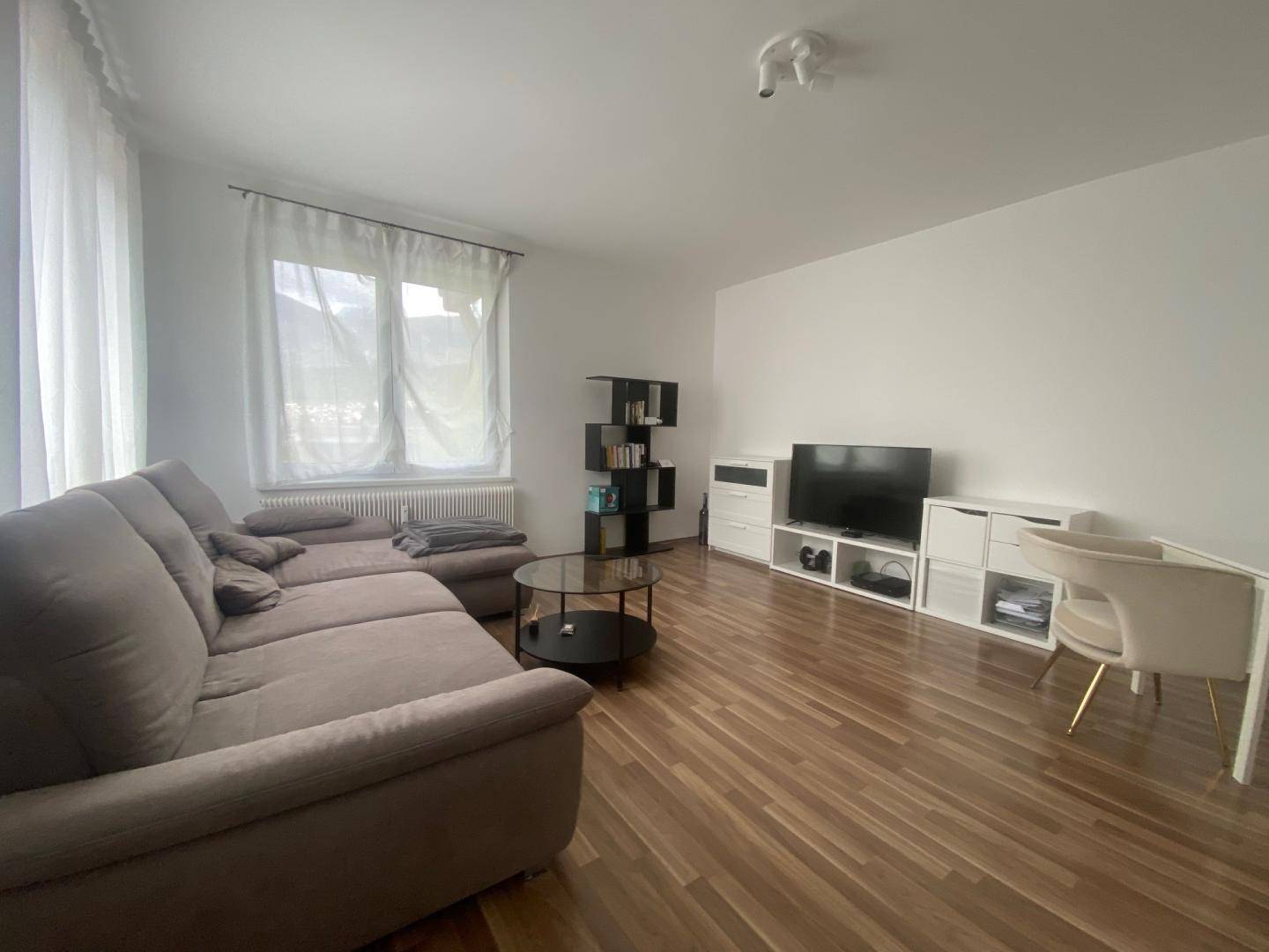 Gemütliches Wohnzimmer mit bequemer Couch, Couchtisch und hellem Laminatboden.