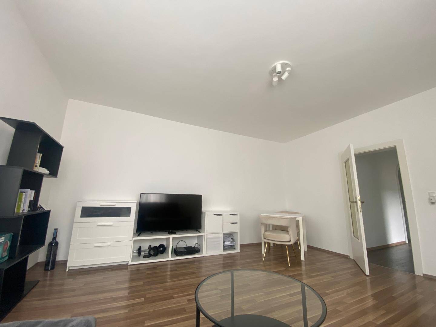 Geräumiges Wohnzimmer mit TV-Möbeln, Bücherregal und Zugang zu einem weiteren Raum.