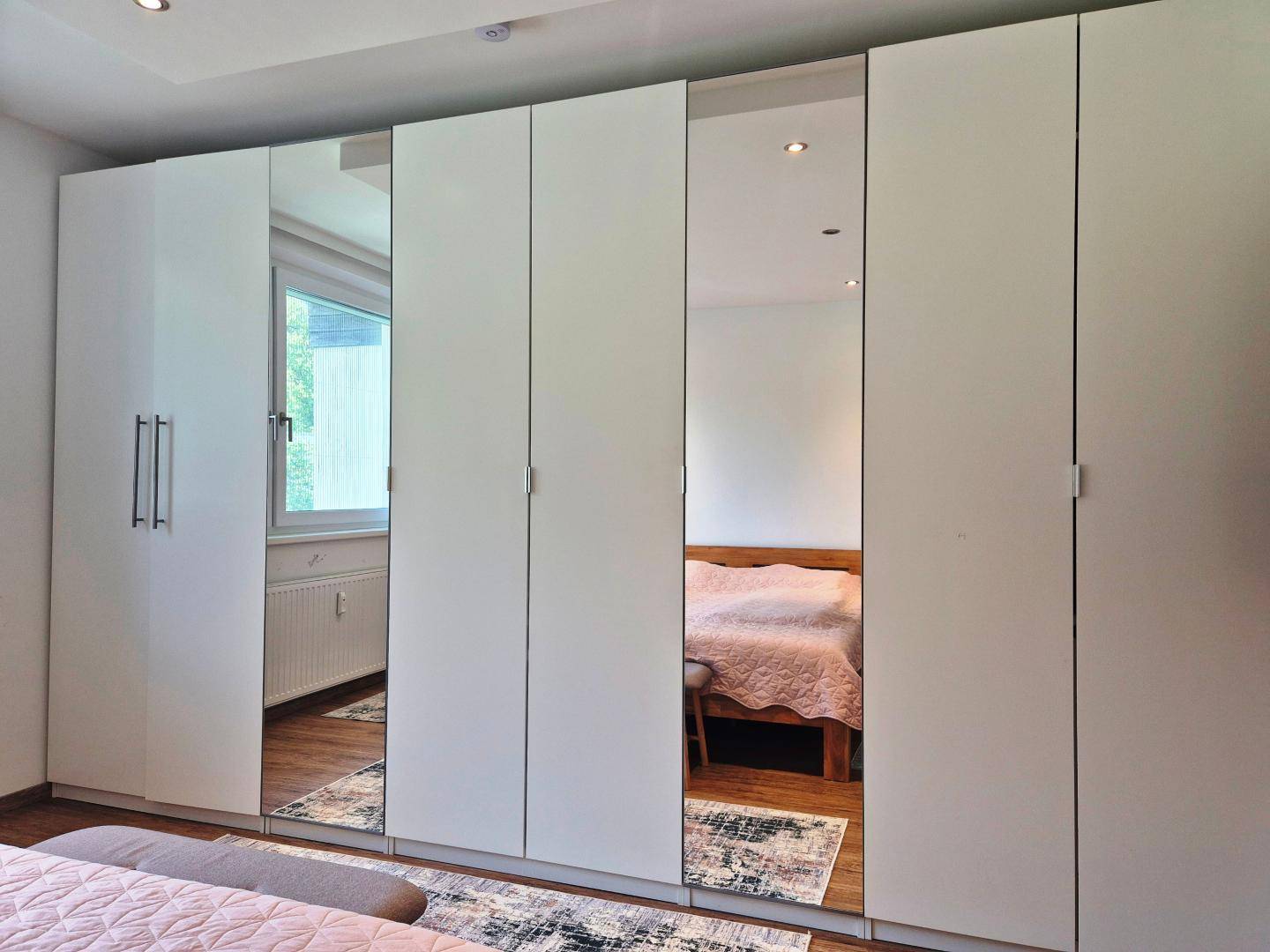 Geräumiger weißer Kleiderschrank mit Spiegeltüren, der das Schlafzimmer optisch vergrößert und aufhellt.