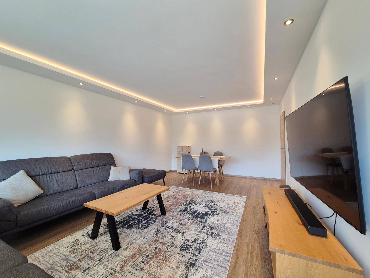 Geräumiger Wohnbereich mit bequemer Couch, Esstisch und moderner Beleuchtung in einem hellen Ambiente.