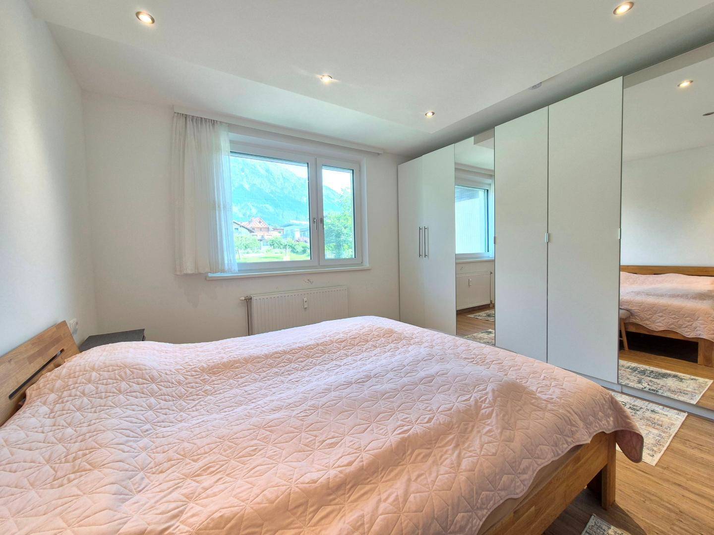 Helles Schlafzimmer mit Holzbett, großem Kleiderschrank und Fenster mit Blick ins Grüne.