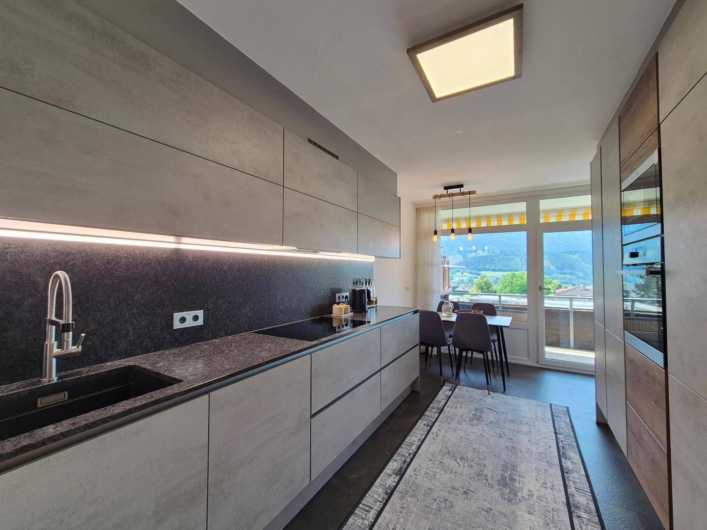 Moderne Einbauküche mit integrierten Geräten, Essbereich und Zugang zu einem Balkon mit Bergblick.