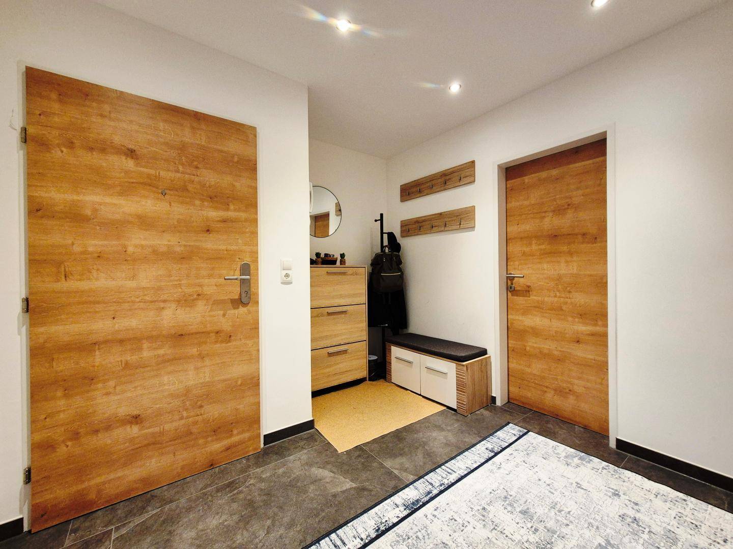 Freundlicher Eingangsbereich mit Holztüren, Garderobe und Sitzgelegenheit, die zum Verweilen einlädt.
