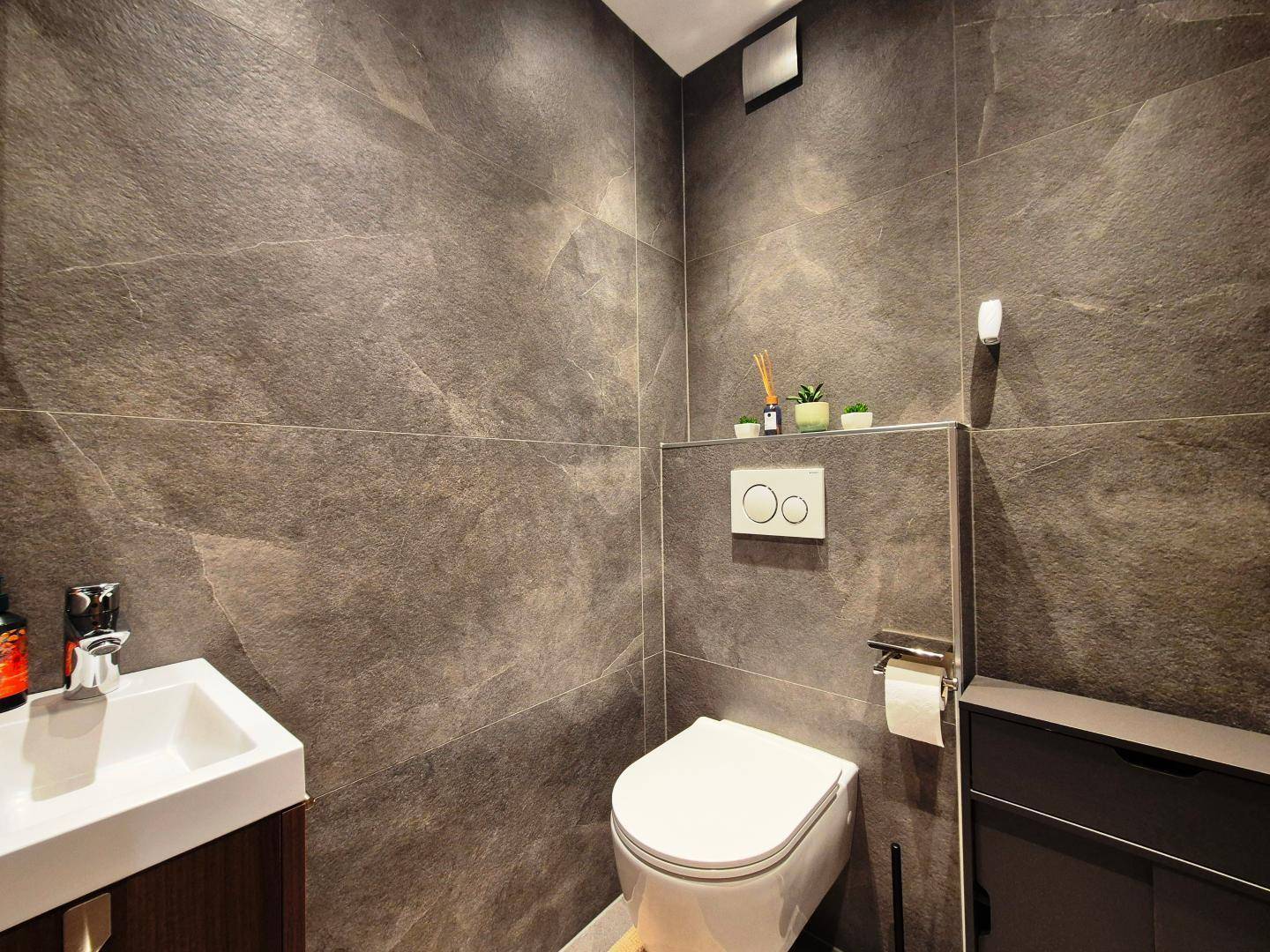 Modernes Gäste-WC mit dunklen Fliesen, wandhängendem WC und kleinem Waschbecken.