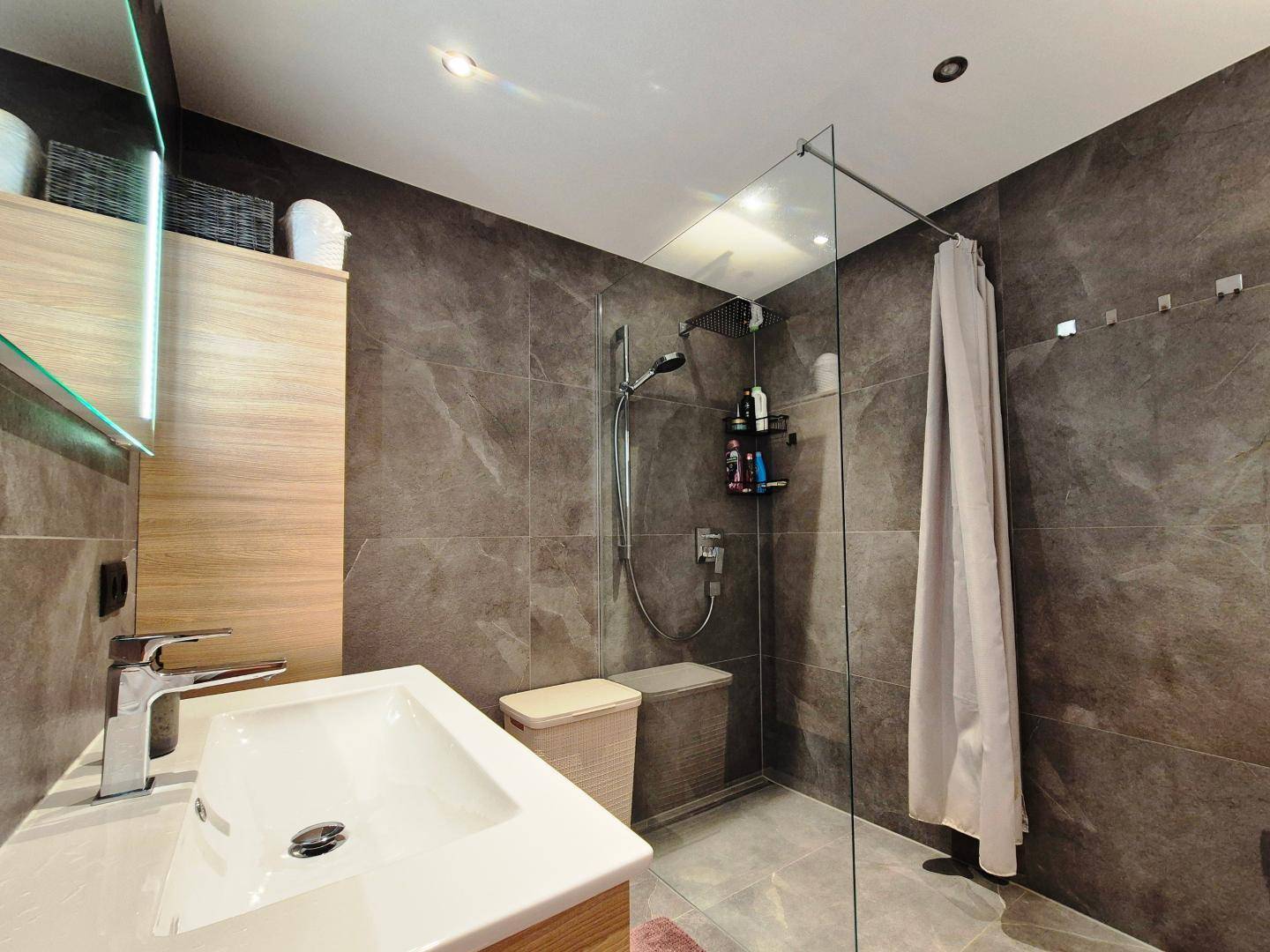 Modernes Badezimmer mit ebenerdiger Dusche, eleganten dunklen Fliesen und einem einzelnen Waschbecken.