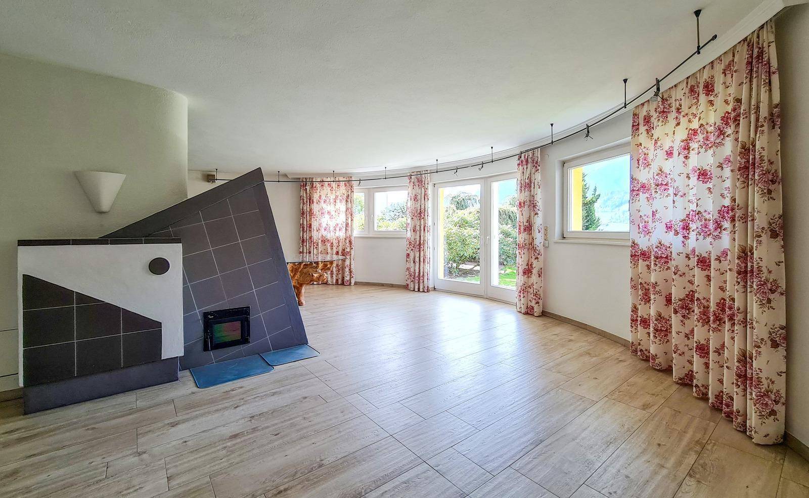 Geräumiges Wohnzimmer mit Kamin, großen Fenstern und floralen Vorhängen, bereit zur individuellen Gestaltung.