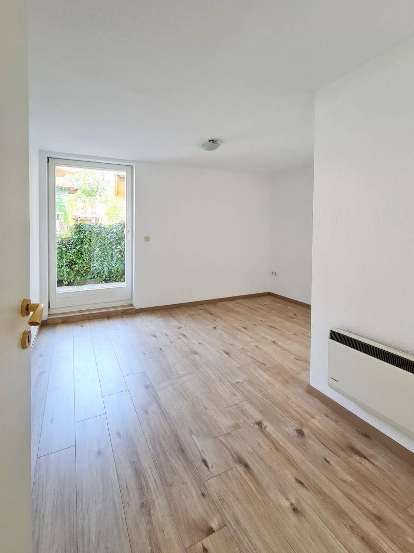 Helles Zimmer mit Holzboden und Zugang zu einem kleinen Außenbereich, ideal als Schlaf- oder Arbeitszimmer.