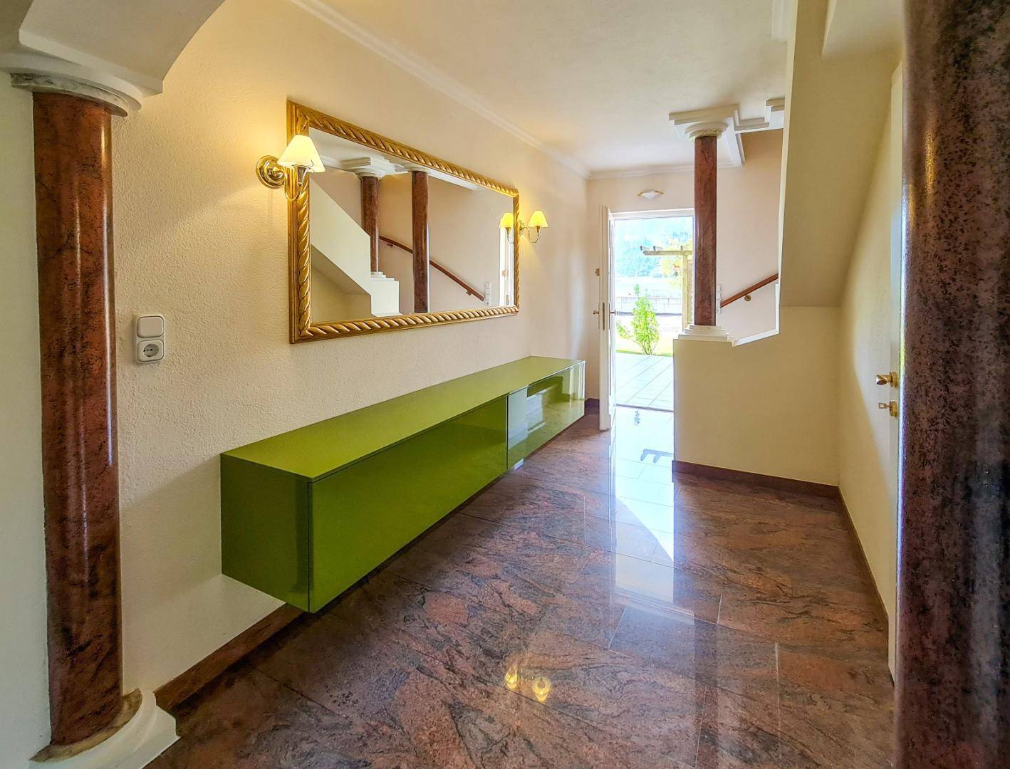 Heller Flur mit glänzendem Marmorboden, einem grünen Sideboard und einem großen Spiegel.